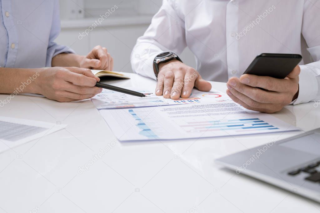 Hands of contemporary economists discussing financial chart on paper while one of them pointing at document