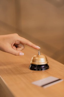 Çağdaş genç iş kadınının eli otel resepsiyonundaki yüzüğün üstündeki çağrı düğmesine basacak.