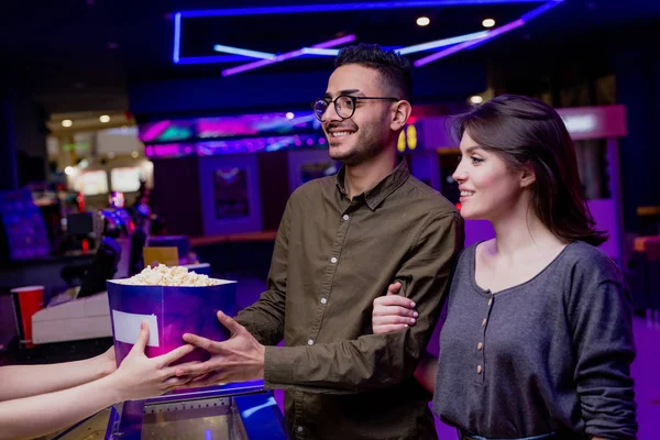 Happy young affectionate couple buying popcorn and tickets in cinema while going to watch movie