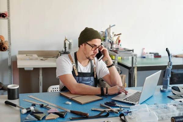 Junge Lederarbeiterin Mit Mütze Und Laptop Telefoniert Mit Kunden Lederprodukte — Stockfoto