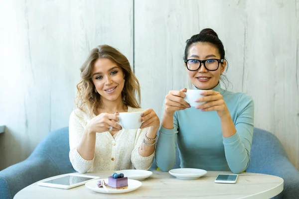 Duas Jovens Fêmeas Interculturais Repousantes Com Xícaras Cappuccino Sentadas Sofá — Fotografia de Stock