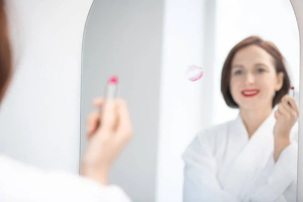 Reflejo Mujer Joven Albornoz Blanco Sosteniendo Lápiz Labial Carmesí Mientras —  Fotos de Stock