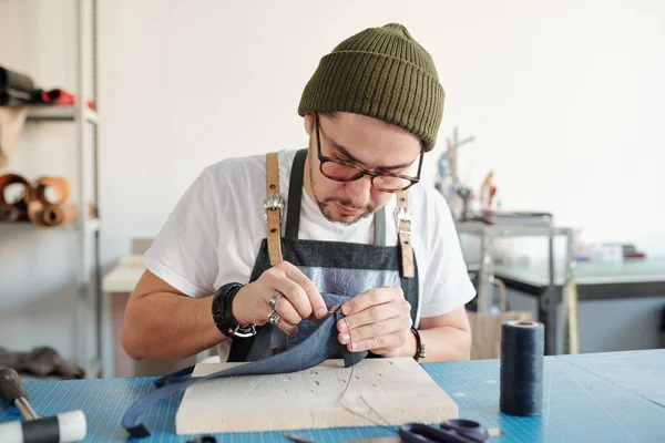 Joven Concentrado Sombrero Sentado Escritorio Cosiendo Cuero Sobre Tabla Madera —  Fotos de Stock