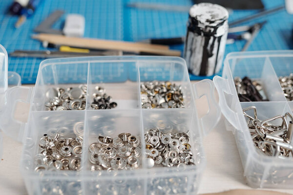 Close-up of transparent containers of rivets and snaps on leatherworkers desk in workshop