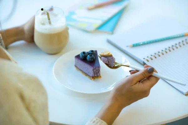 カフェでカプチーノとデザートを楽しみながら プレートの上においしいブルーベリーチーズケーキの作品とフォークを保持女の子の手 — ストック写真