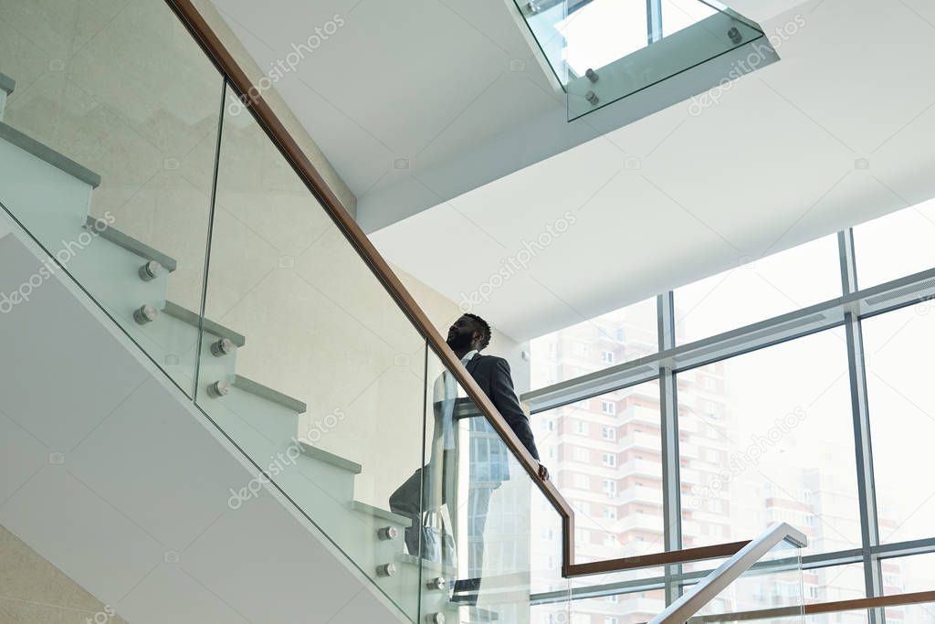 Young contemporary African businessman in elegant suit going upstairs to his office inside large business center