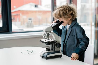 Laboratuvarda çalışırken mikroskop altında masasında kıvırcık saçlı zeki bir öğrenci.