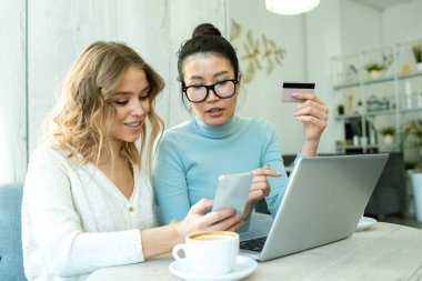 Şirin bir kız, sipariş vermeden ve parasını ödemeden önce arkadasina akıllı telefondaki kozmetik ürününü gösteriyor.