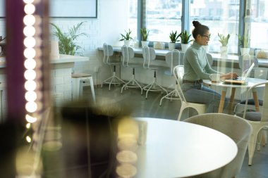 Küçük kafeteryada bir fincan kahve içerken dizüstü bilgisayarın önünde oturan genç Asyalı serbest çalışan kadın.