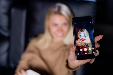 Yüz maskesi filtresiyle multimedya uygulaması kullanırken akıllı telefonu kamerayla değiştiren genç sarışın kadının eli