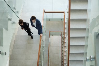 Çağdaş ofis binasında resmi giyinmiş iki genç iş adamının üst katta yürümesi