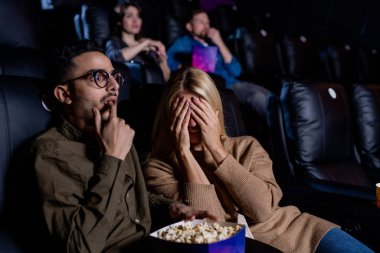 Genç, korkmuş bir kadın, erkek arkadaşıyla korku filmi izlerken yüzünü kapatıyor ve sinemada patlamış mısır yiyor.