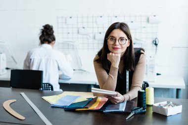 Elbise tasarım stüdyosundaki tekstil desenli masaya yaslanan çekici kadın portresi