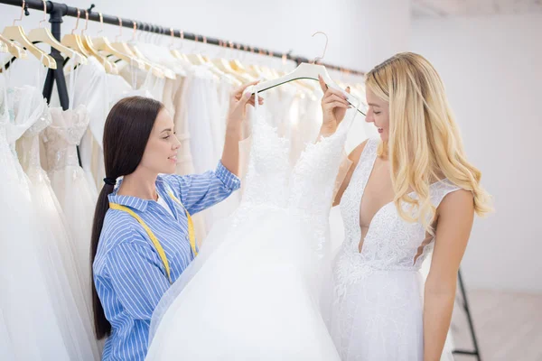 Позитивная Блондинка Невеста Выбирает Свадебное Платье Примерки Консультантом Магазине — стоковое фото