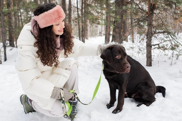 Όμορφη Νεαρή Μελαχρινή Χειμερινά Ενδύματα Κοιτάζοντας Μαύρο Retriever Κάθεται Στο — Φωτογραφία Αρχείου