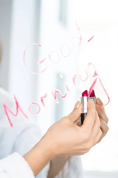 鏡の近くに紅色の口紅を持っている若い女性の手は良い朝を書きながら — ストック写真