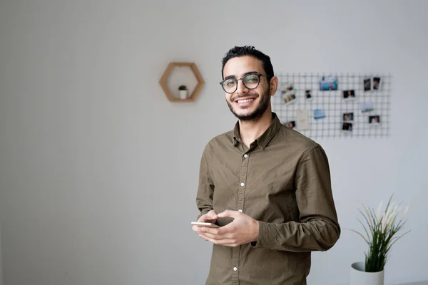 Ofiste Kameranın Önünde Dikilirken Akıllı Telefondan Kayan Dişlek Gülüşlü Genç — Stok fotoğraf