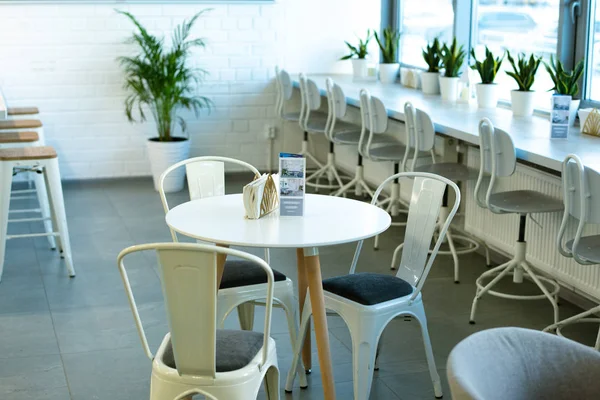 White round table and three chairs around on background of windowsill and green domestic plants in cafeteria