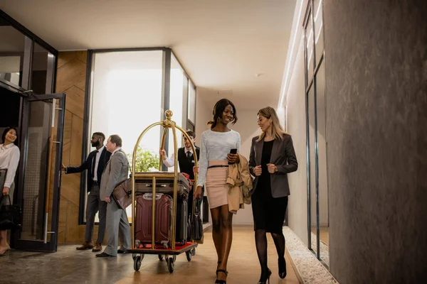 ホテル内に荷物を持ち運ぶポーターと移動中に通信している異文化ビジネス旅行者 — ストック写真