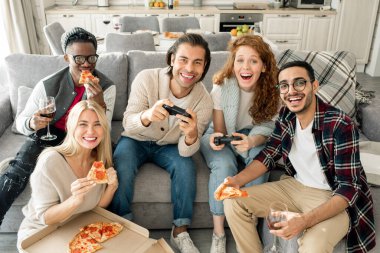 Beş farklı etnik gruptan arkadaş pizza yiyip video oyunu oynayarak eğleniyorlar. Kameraya yatay olarak bakıyorlar.