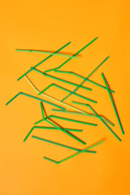 Vertical conceptual flat lay image of disposable plastic drinking straws on bright orange background