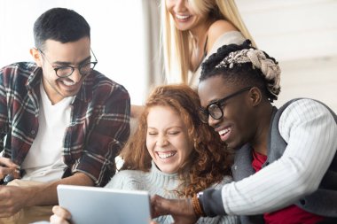 Çevrimiçi videoya gülerken tablet kullanan bir grup neşeli çoklu etnik arkadaş