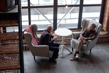 Orta yaşlı şık işadamları rahat koltuklarda oturuyor ve lobi barında alkol içiyor.