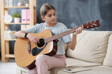 Kanepede oturan ve gitar çalmayı öğrenirken interneti tablette kullanan mutlu genç kız.