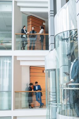 Genç ofis çalışanı balkonlarda duruyor ve modern finans bölgesinde iş tartışıyor.