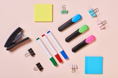 Highlighter pens, whiteboard markers, paper clips and sticker papers on pale pink background, flat lay shot