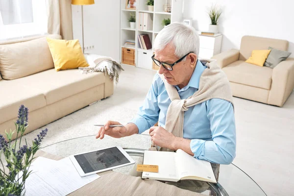 当代退休男子 坐在家中的桌子旁 手里拿着数码平板电脑和银行卡 在线订票 — 图库照片