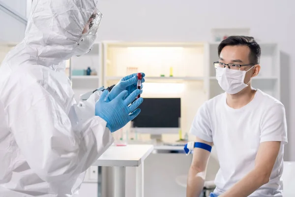 Medical Specialist Protective Suit Talking Asian Patient While Taking Blood — Stockfoto