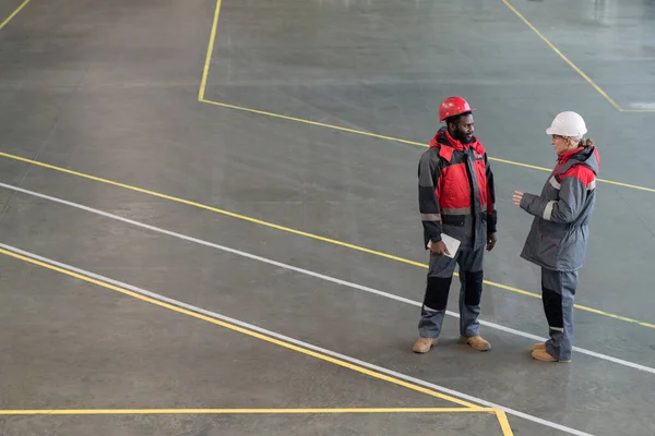 两名穿着制服站在一起聊天的年轻成人工厂工人的横向高角镜头 — 图库照片