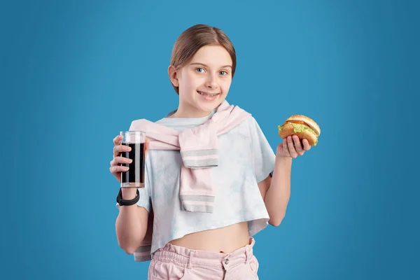 Retrato Adolescente Positiva Comendo Hambúrguer Insalubre Bebendo Cola Contra Fundo — Fotografia de Stock