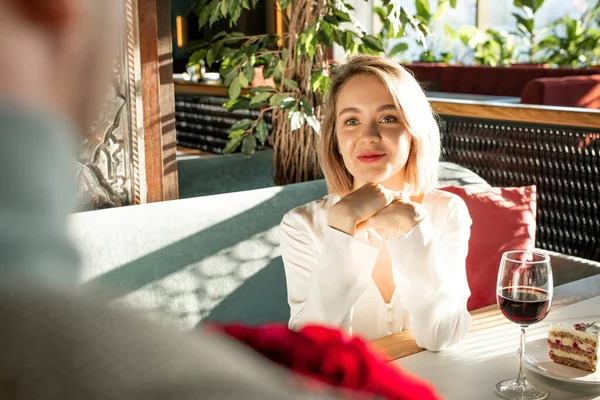 Over-the-shoulder shot of young blond woman sitting in front of man in restaurant flirting with him