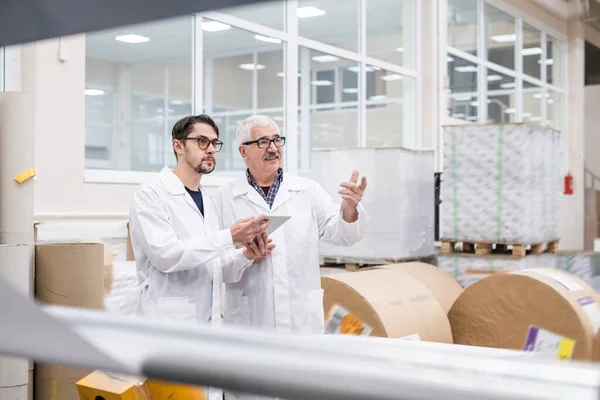 高级和年轻的白衣实验室专家在工厂使用数码平板电脑 同时谈论工业生产力 — 图库照片