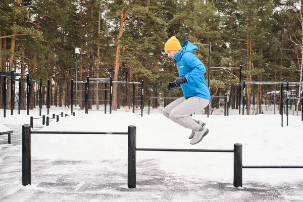 Mavi Ceketli Bir Gencin Kışın Atlamak Için Yatay Çubukları Kullanışının — Stok fotoğraf