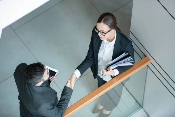 Above view of businessman with tablet handshaking with female analyst after negotiations