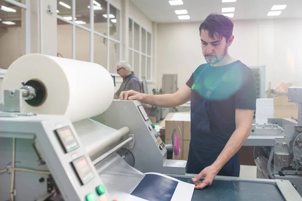 严重的年轻印刷专家与胡子操作印刷机同时在工厂打印测试页 — 图库照片