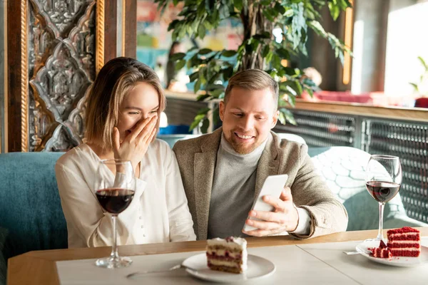 水平拍摄的年轻男女坐在咖啡馆桌旁 一边看智能手机上有趣的东西 一边笑 — 图库照片