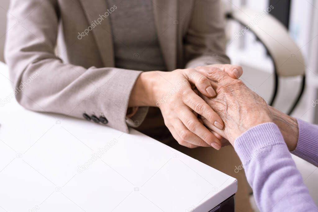 Close-up of unrecognizable social worker holding hands of elderly woman while supporting her