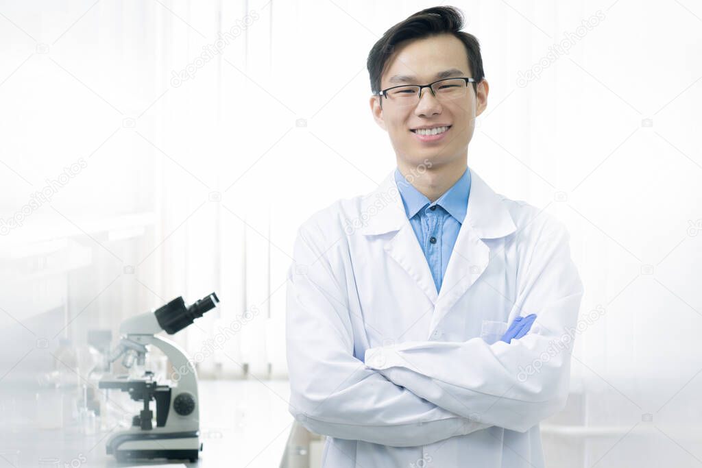 Confident Asian man wearing white lab coat and eyeglasses standing with arms crossed looking at camera smiling