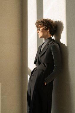 Güneş ışığında duvarda duran siyah elbiseli çekici genç iş kadını.