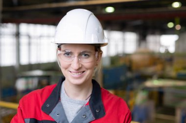 Portrait of positive female industrial worker in safety goggles and work helmet at factory