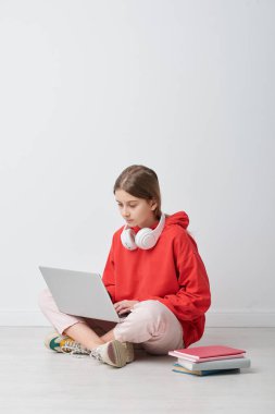 Boynunda kablosuz kulaklıkları olan meraklı bir öğrenci dizüstü bilgisayarında online iş yapıyor.