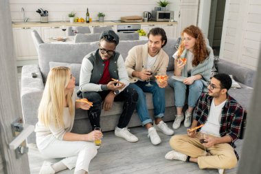 Genç erkek ve kadınların, modern bir dairede pizza yiyip sohbet ederken geçen yatay yüksek açı çekimleri.