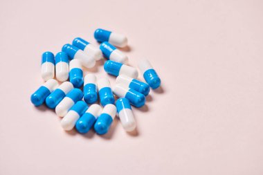 Blue and white capsules on pale pink surface, horizontal close up shot