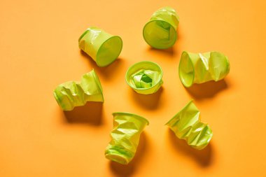 Used disposable light green plastuc cups lying on bright orange surface, horizontal high angle shot