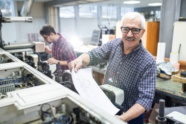 Gözlüklü neşeli son sınıf öğrencisinin portresi. Fabrikadaki matbaadan basılı kağıt alıyor.