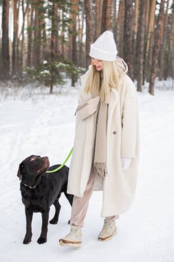 Sahte kürk giyen genç bir kadının kış günü güzel köpeğiyle dışarıda vakit geçirdiği yatay bir fotoğraf.